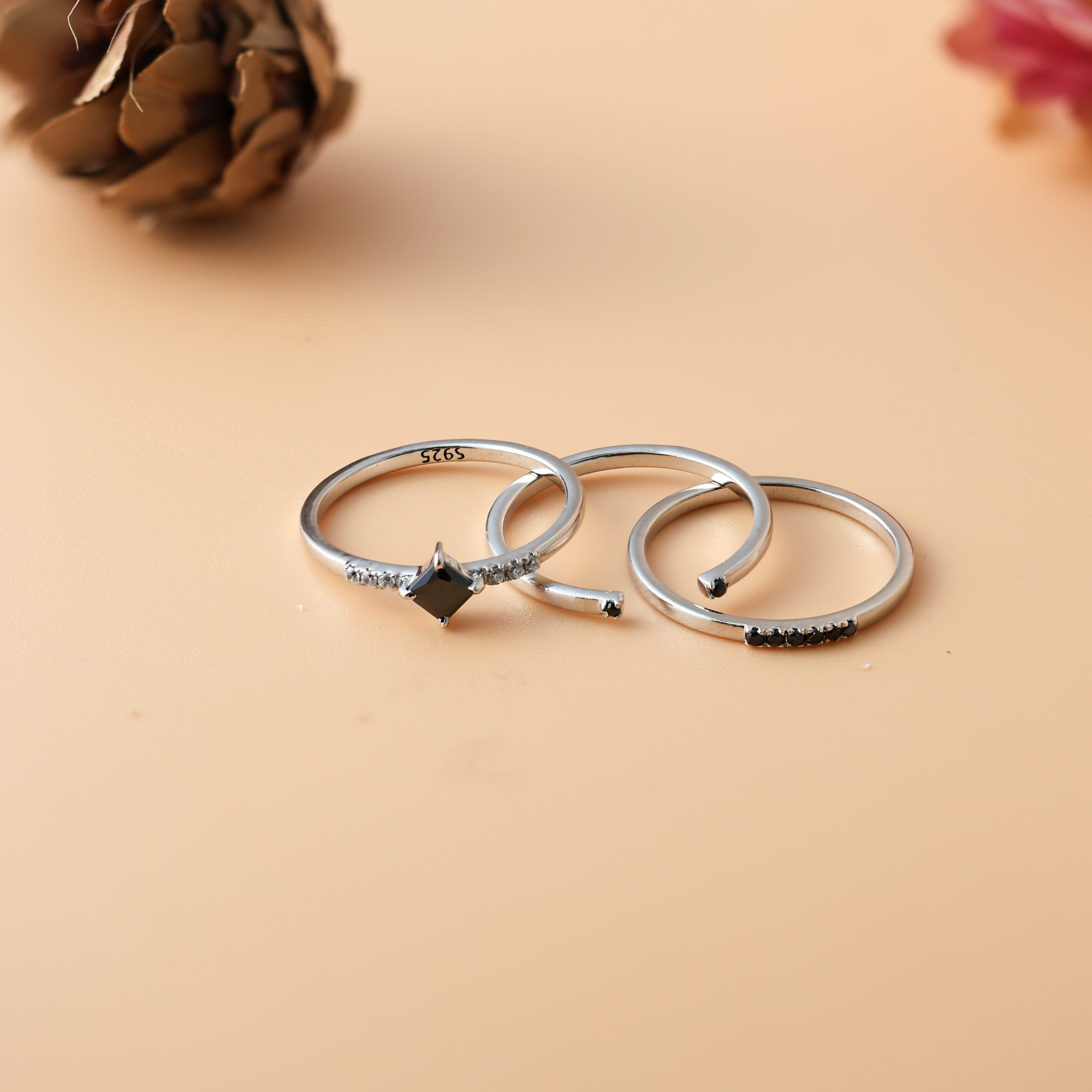Three silver rings with black accents on a beige background